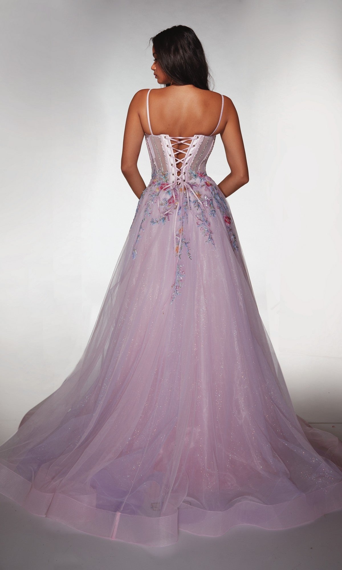 A woman stands facing away against a plain backdrop wearing the Alyce 62068, a long light purple prom dress with a floral corset bodice, lace-up back, and sleeveless design.